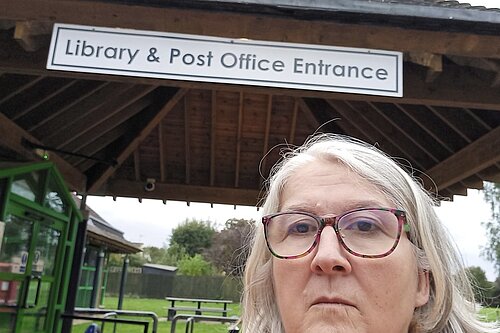 Edna Murphy in front of a sign saying "Library & Post Office Entrance"