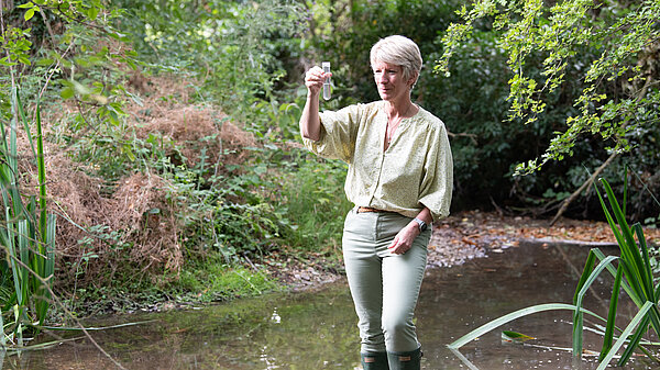 Pippa Heylings, Lib Dem parliamentary candidate for South Cambs, standing in a chalk stream, looking at a test tube full of polluted water