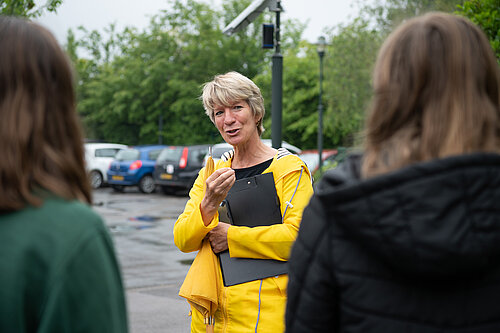 Pippa Heylings talking to two local residents, standing in a car park in the rain