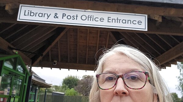 Edna Murphy in front of a sign saying "Library & Post Office Entrance"