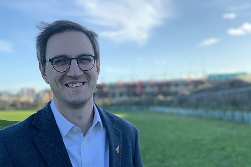 Ian Sollom standing in a field with new housing in the distance